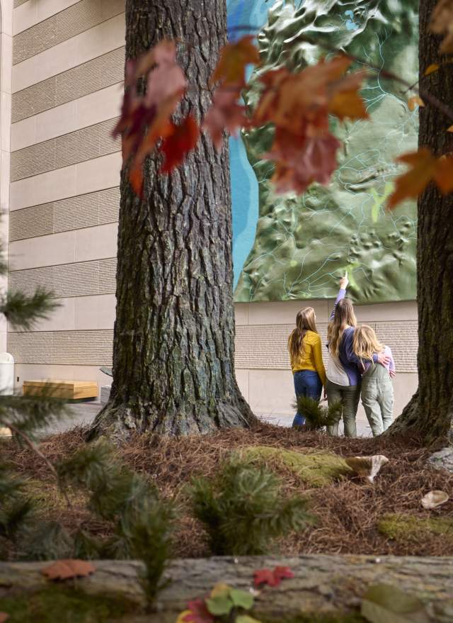 A woman and two children looking up at a giant topographical map of Michigan.