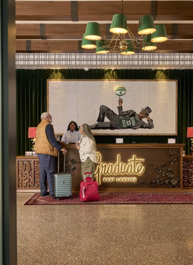 A couple at the front desk of the Graduate Hotel, preparing to check in with their luggage.