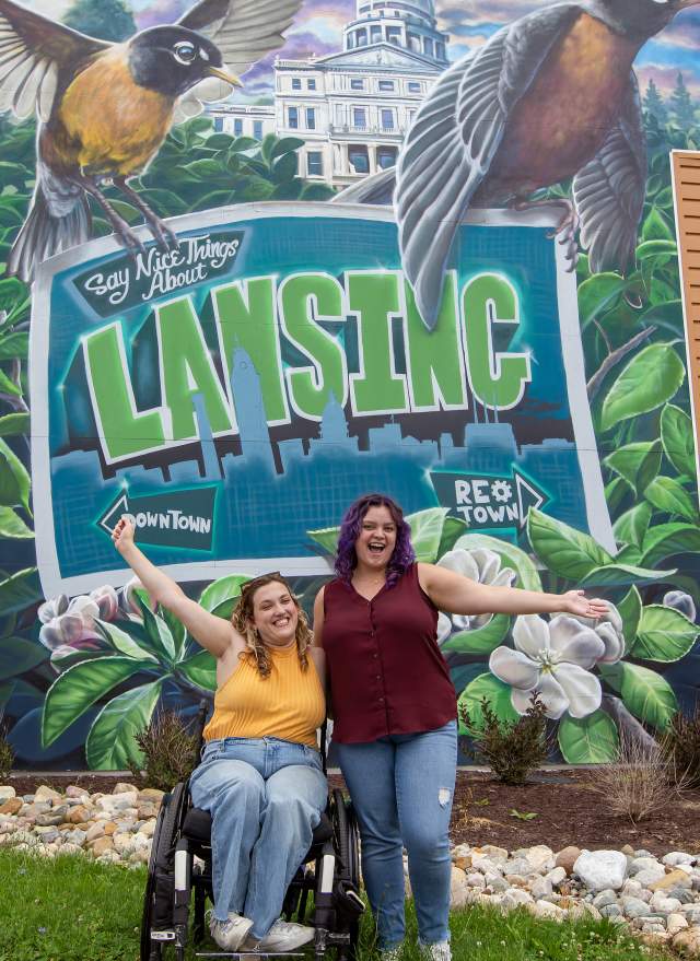 Two ladies in front of a "Say Something Nice Mural Lansing"