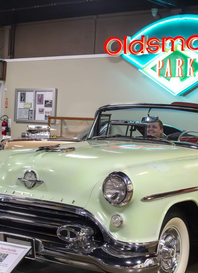 Couple sits inside old convertible while another person takes their photo
