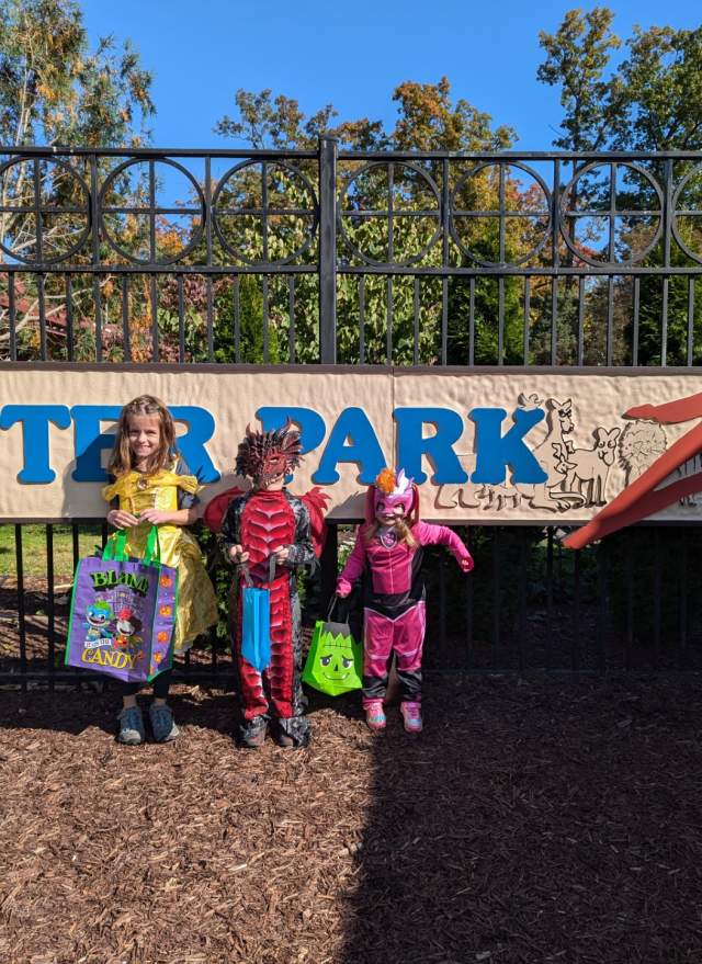 Three kids dressed in halloween costumes in front of the Potter Park Zoo sign