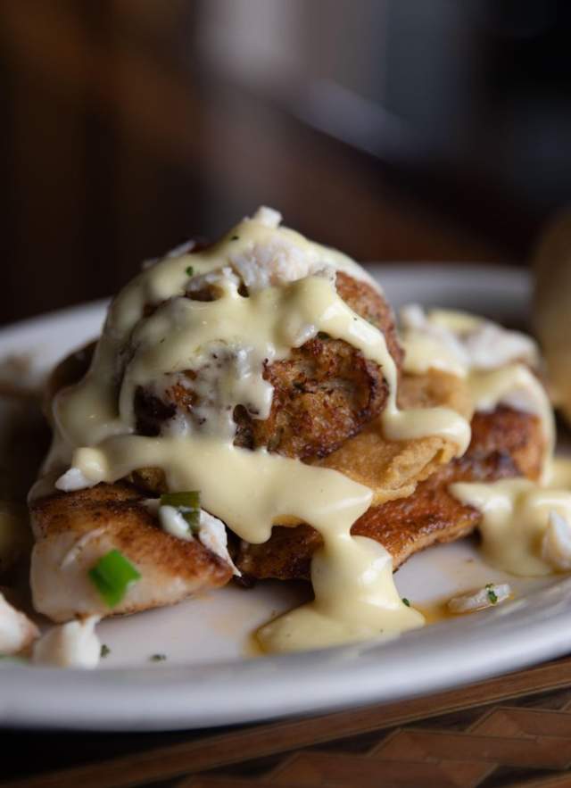 Blackened fish with cream sauce and lump crab meat and a roll on a white oval plate