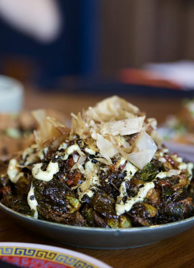 Bowl of wok-fried brussel sprouts sitting on table with other appetizers in the background.
