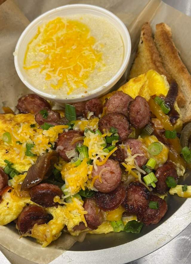Omelet on a plate with sausage, cheese, green onions, toast and grits topped with cheese