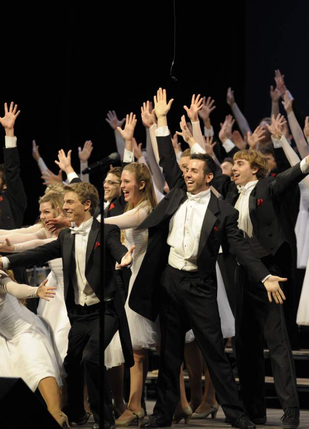 The Singing Hoosiers performing on stage at Indiana University in Bloomington, Indiana, featuring a large ensemble in formal attire singing and dancing under stage lighting.