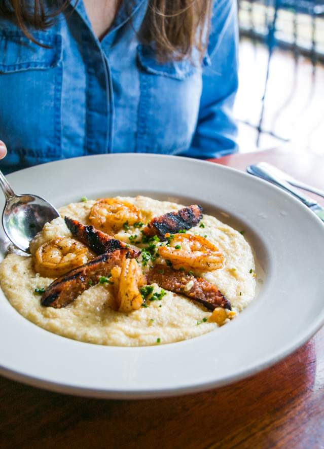 Woman sitting in front of a bowl of shrimp and grits at Uptown