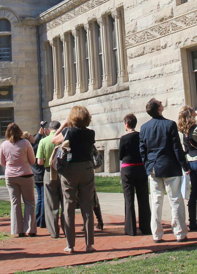 Group Travel in Bloomington guided tour, observing and pointing at historic stone buildings on a sunny day.