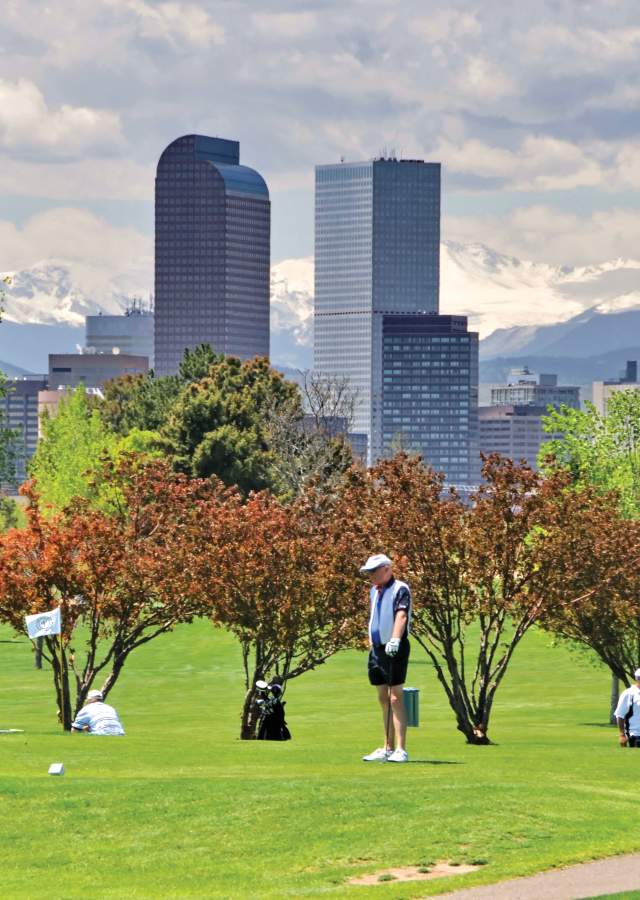 Golfers at City Park with Denver skyline and mountains.