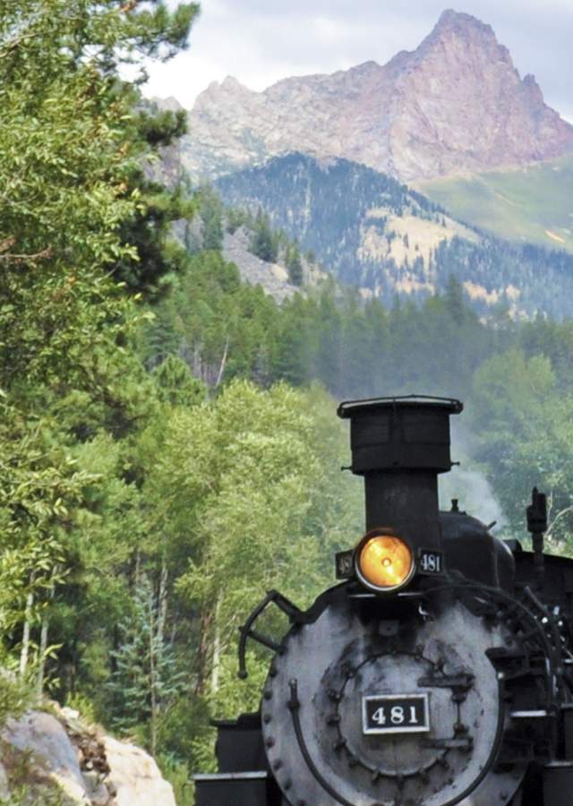 A Durango & Silverton Narrow Gauge Railroad train makes its way up the tracks with mountains in the background.