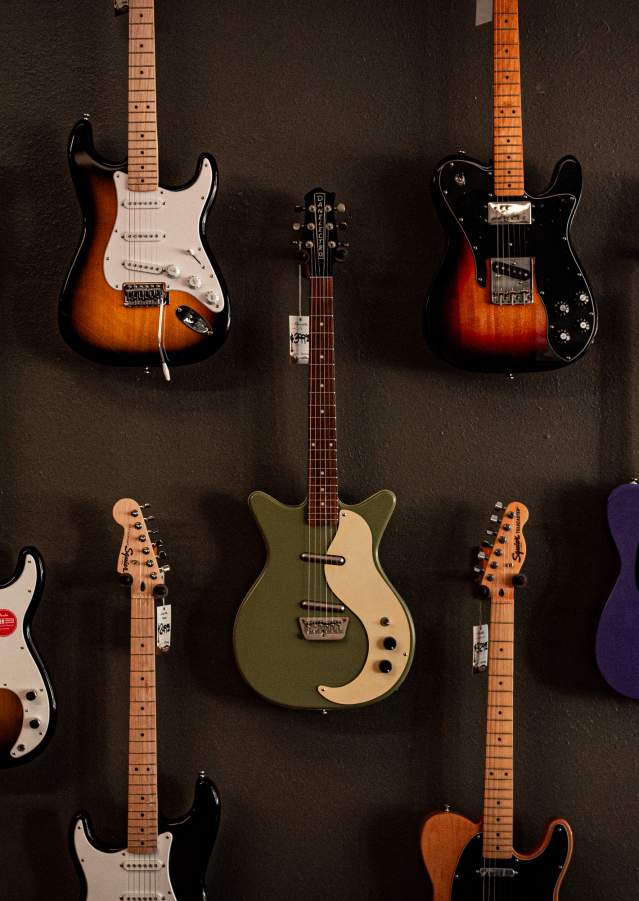 A variety of electric guitars are hanging on a dark gray wall.
