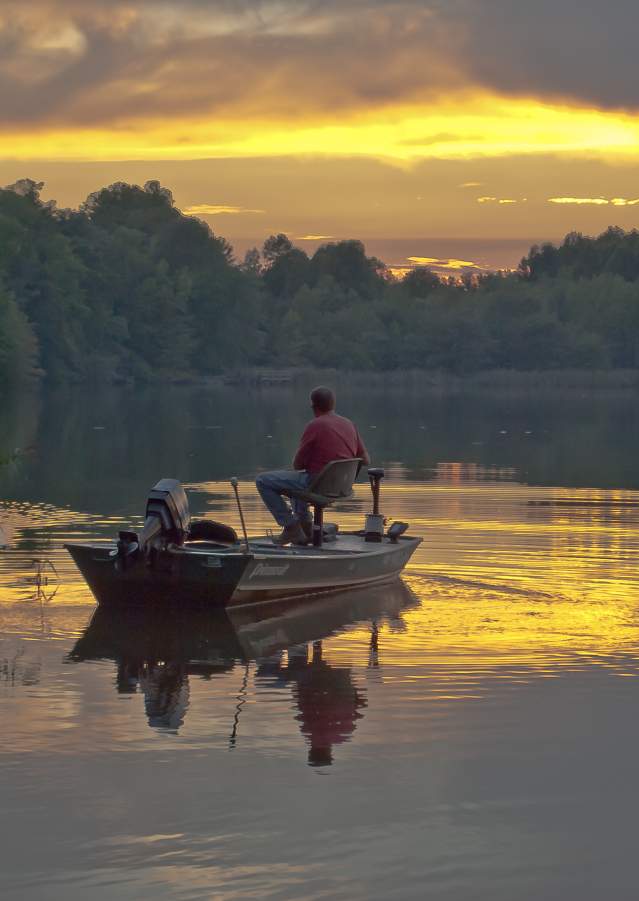 A fisherman enjoys the morning sunrise over the water at Lums Pond State Park.