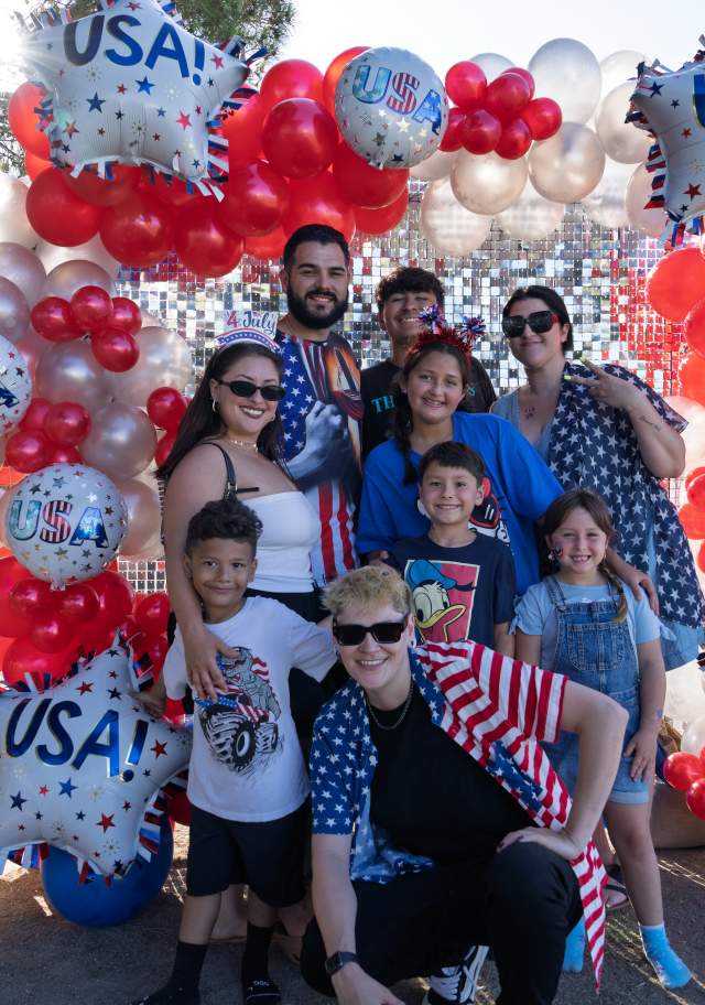 Families pose beneath a patriotic red, white, and blue balloon arch during the Santa Ana 4th of July Celebration at Centennial Park in Santa Ana, California.