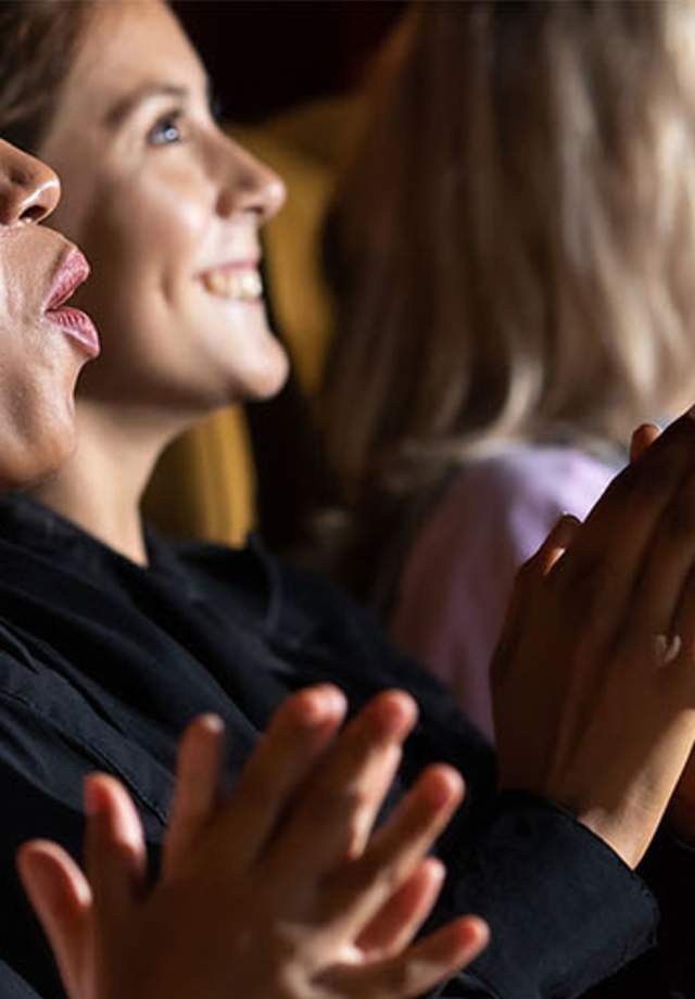 A group of girls and women applauding while watching a movie in an auditorium.
