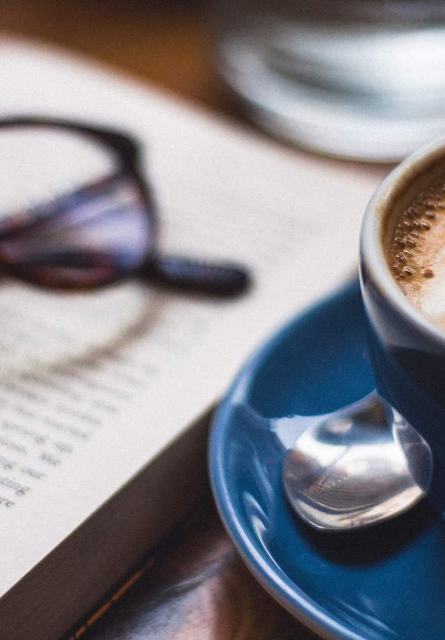 Coffee mug next to a book and reading glasses at a coffee shop - photo by harry-brewer