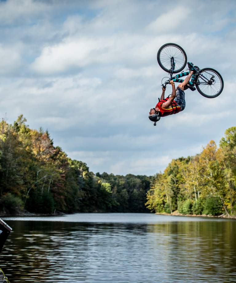 Stunt biker going off a ramp and flipping upside down over water at Griffin Bike Park, Terre Haute, Indiana