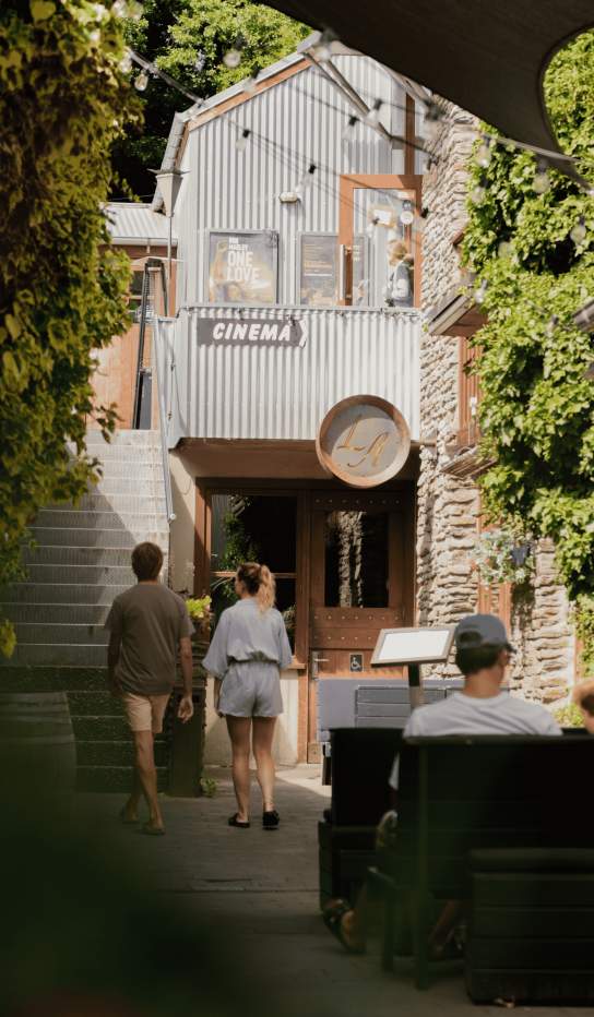 People walking down a side street in Arrowtown with stone buildings and greenery surrounding them