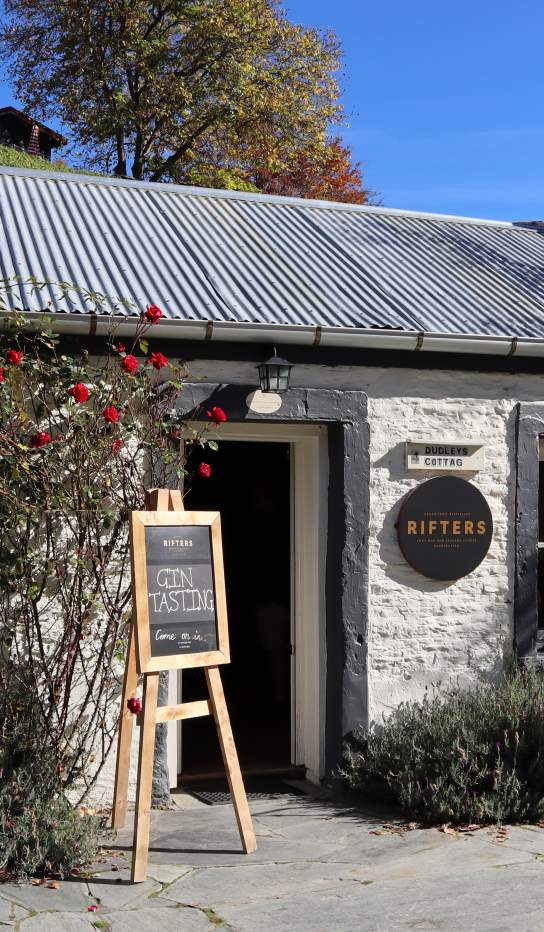 The outside of a white brick cottage with signs out the front for gin tasting