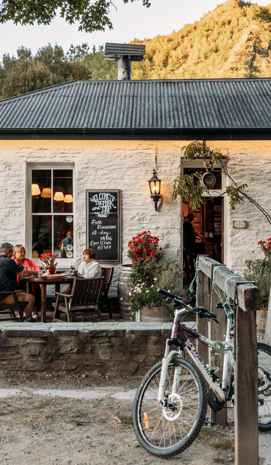 Old white cottage-looking pub with people sitting al fresco and green mountains in the background