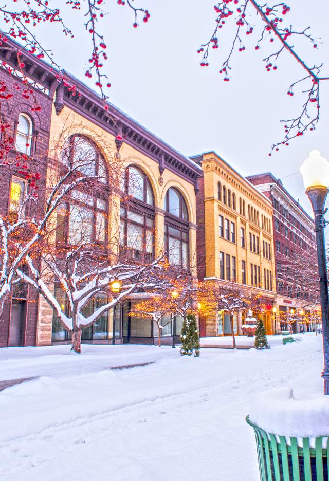 Beautiful varieties of architectural buildings line a downtown that is covered in a fresh white snow.