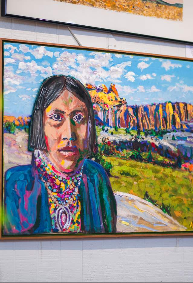 Colorful painting of a native american in the foreground looking at the viewer from a colorful landscape