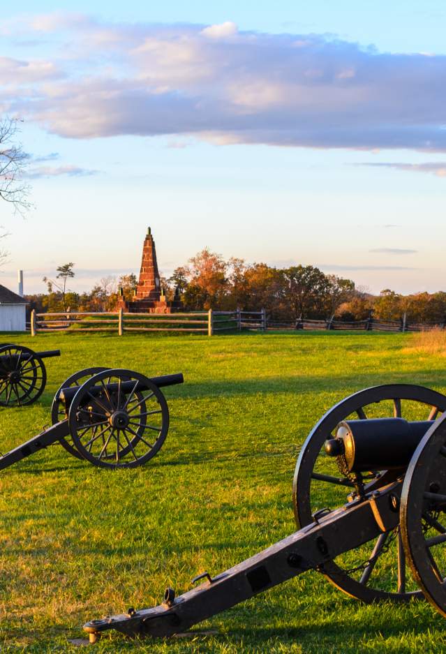 3 cannons on a battlefield with a historic building in the background