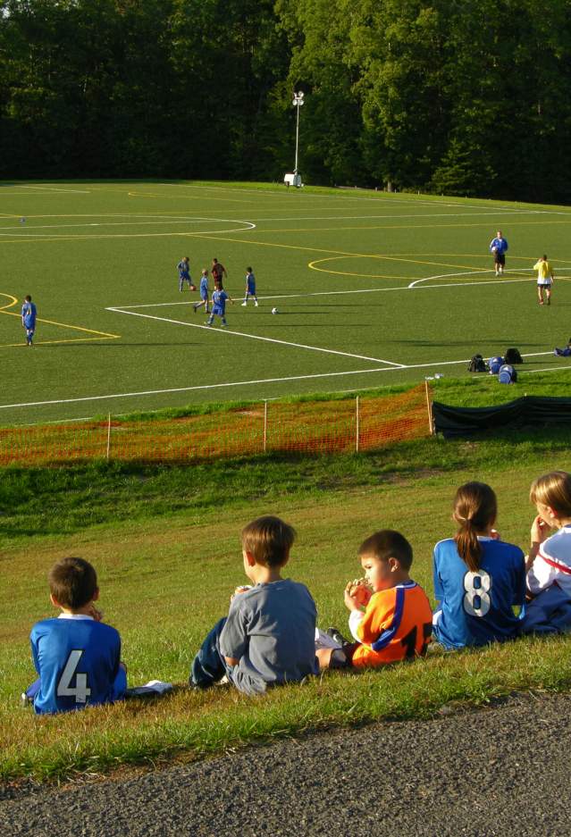 children sitting on a hill watching a soccer game