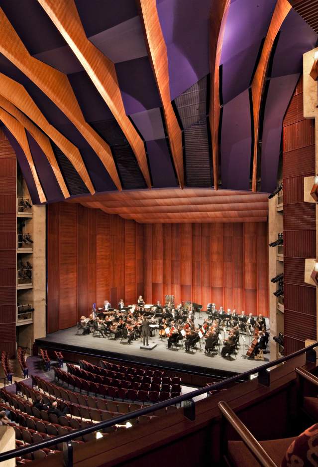 A view of a stage in a theater from the balcony on stage left, on the stage is an orchestra performing