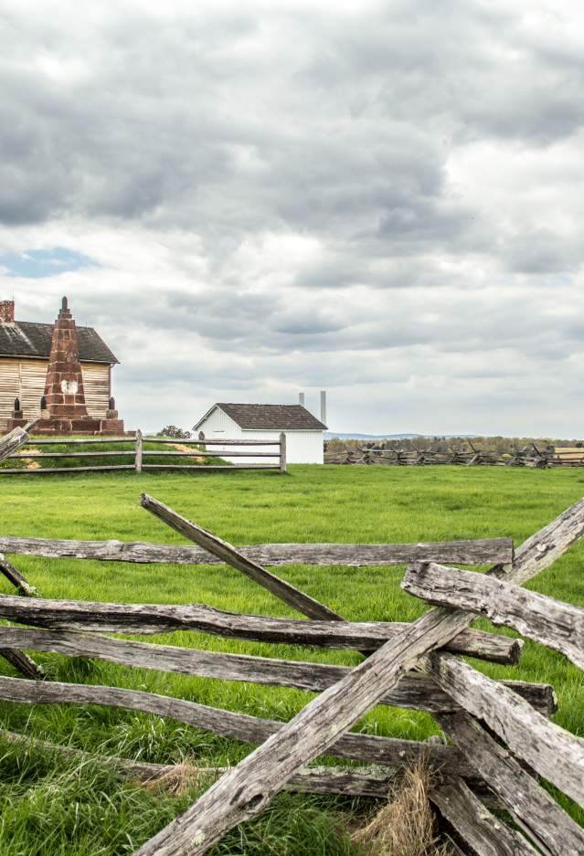 A battlefield with a wooden fence and a historic building in the background