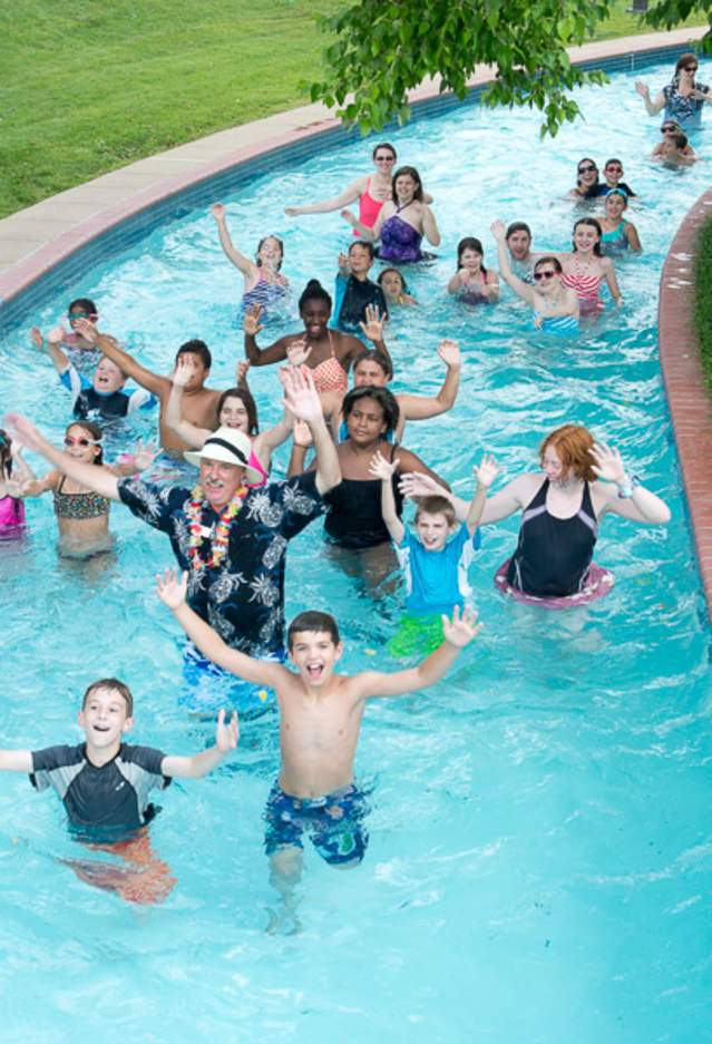 People of all ages in a lazy river with their hands up smiling
