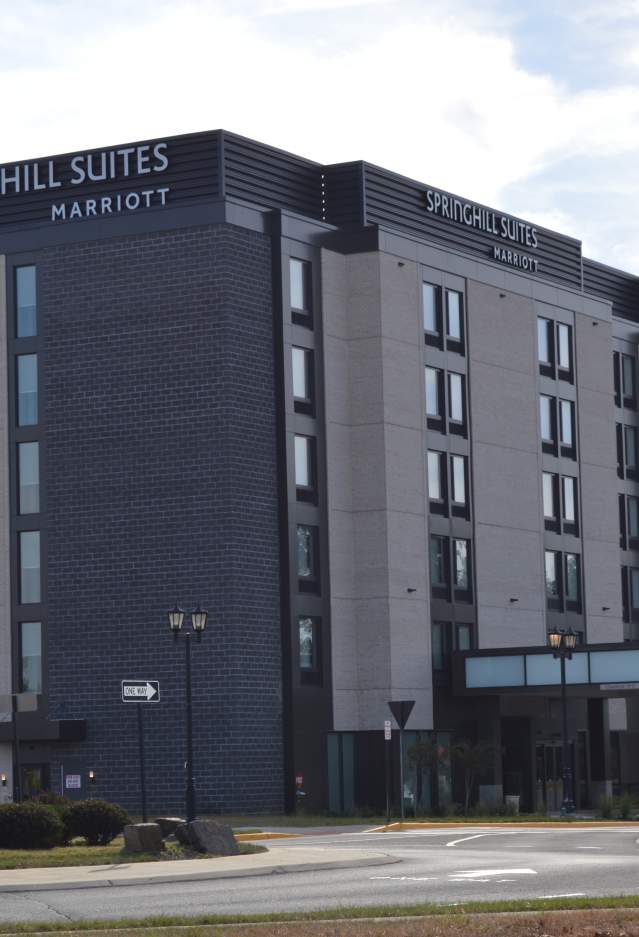 a hotel with black and grey bricks with a driveway and small trees in the front