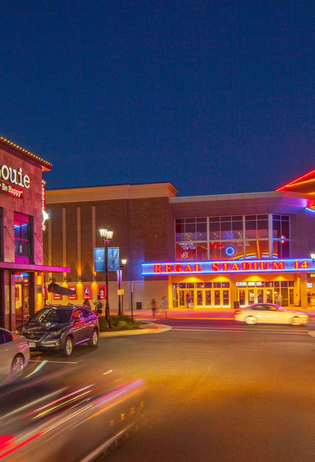 A shopping area at night with neon lights and cars going by