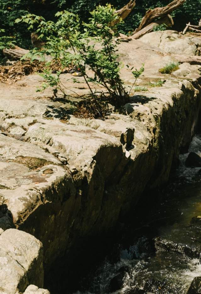 A woman and a man sitting on the edge of a rock along water