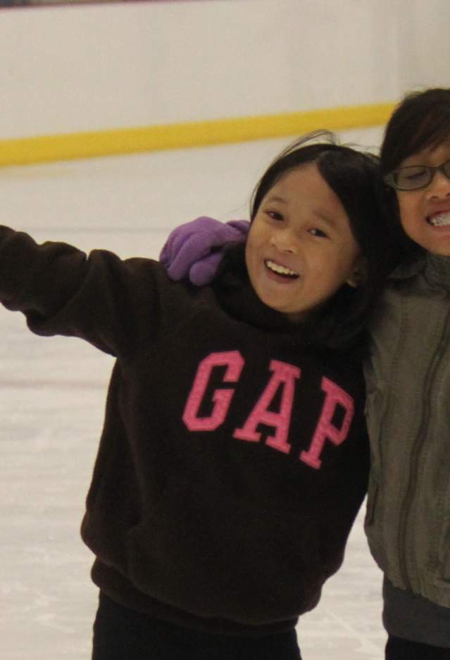 Two girls hugging and holding up peace signs at an ice skating rink