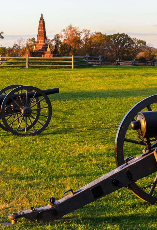 Three cannons on a battlefield with a historic house in the background