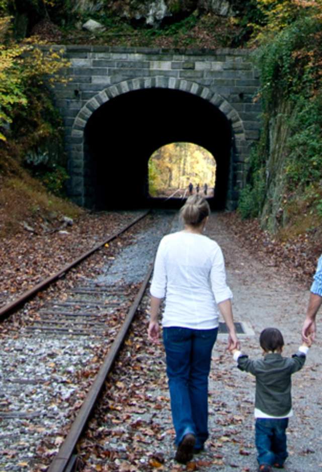 A small child holds hands with their parents as they walk along the rail trail toward Howard Tunnel in fall