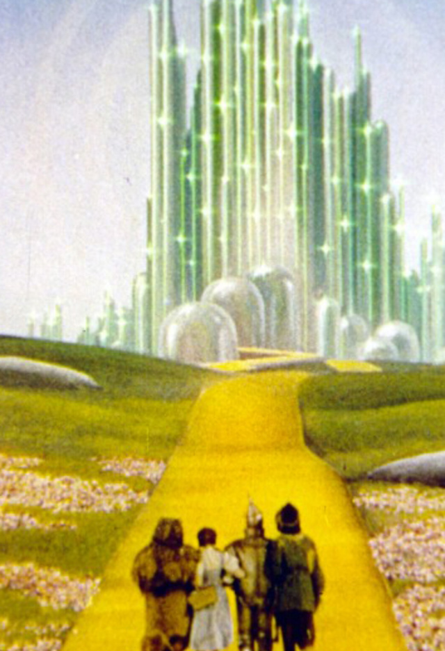 Scene from The Wizard of Oz showing Dorothy, the Scarecrow, the Tin Man, and the Cowardly Lion walking along the yellow brick road toward the shining Emerald City surrounded by green fields and distant cliffs.