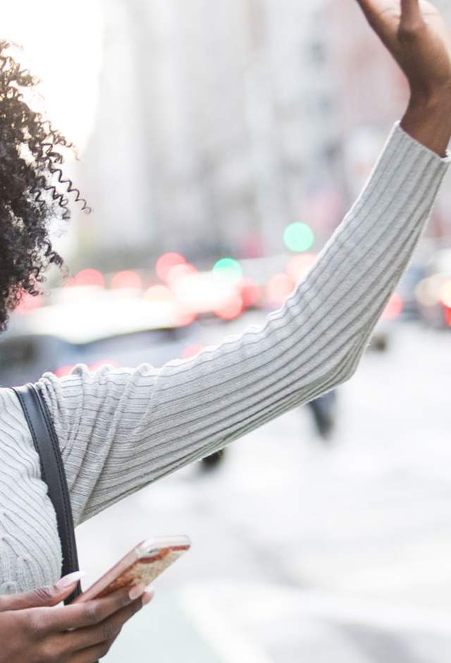 getting here woman signaling for a car while holding her phone