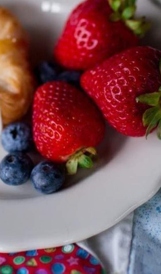 book next to plate of pastry and fruit on bed