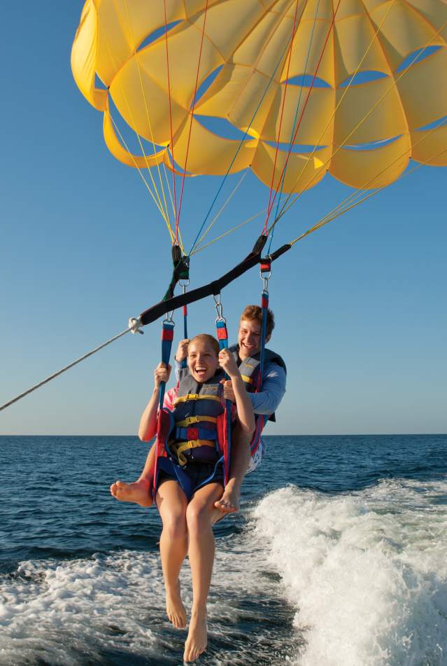 Two people parasailing just above foamy water