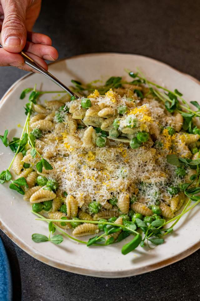 Spoon scooping a large spoonful of tiny pasta with lemon zest, microgreens and a heavy dusting of parmesan cheese.