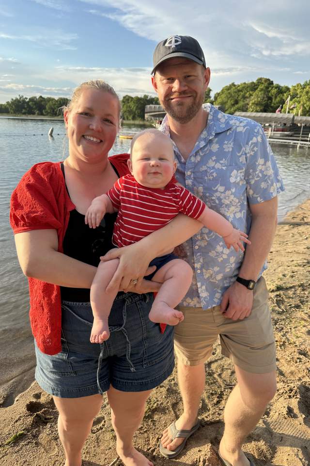 Mother, Father and baby posing in front of a lake in the sand.