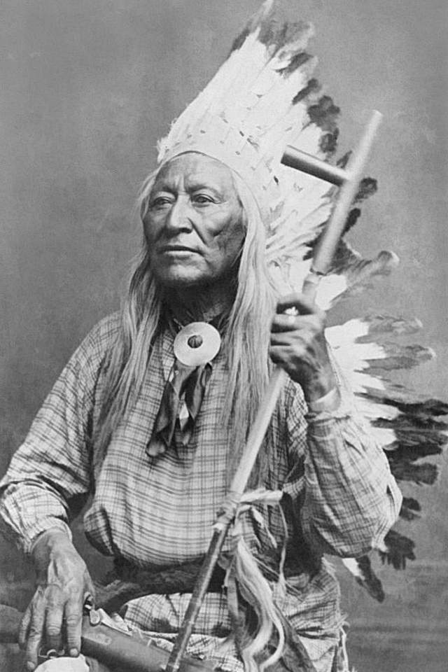 Black and white portrait of Chief Washakie wearing a feathered headdress and holding a ceremonial pipe.