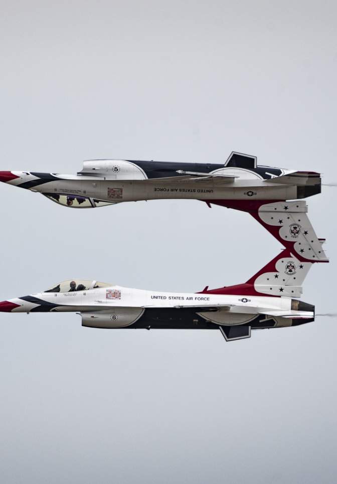 Two jet aircraft flying inverted in close formation above the Fort Lauderdale shoreline, trailing white smoke against a cloudy sky during an air show.