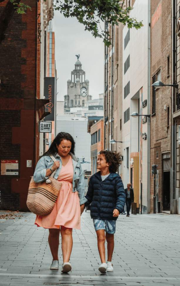People are walking down a street in Liverpool city centre. They are laughing together and the Royal Liver Building is framed in the background of the shot