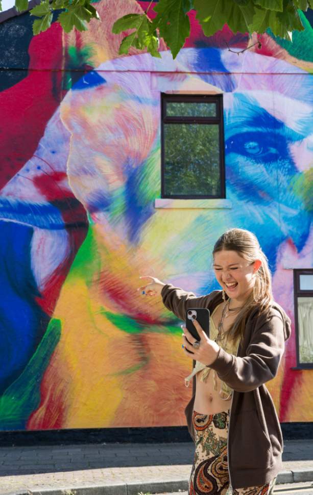 A girl takes a selfie in front of vibrant street art in New Brighton