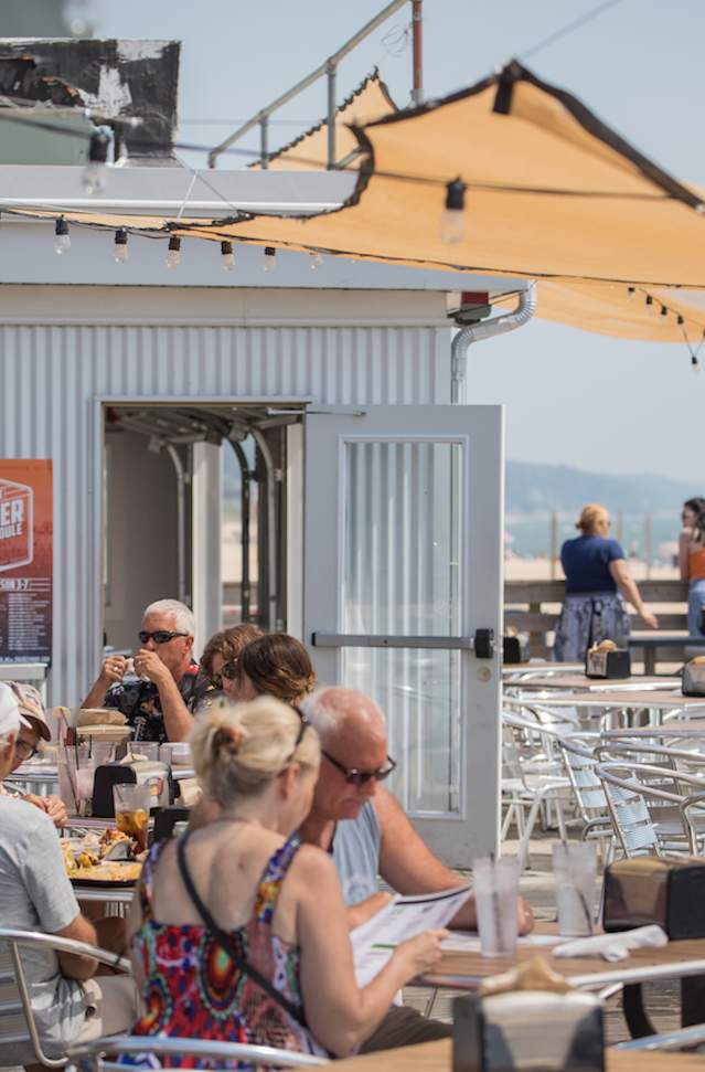 People sitting on outside deck restaurant, under sail canopy.