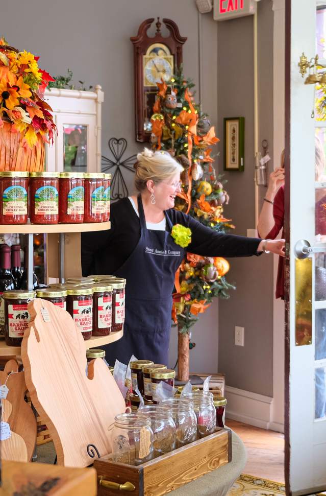 smiling woman opens door to her shop that is decorated for fall