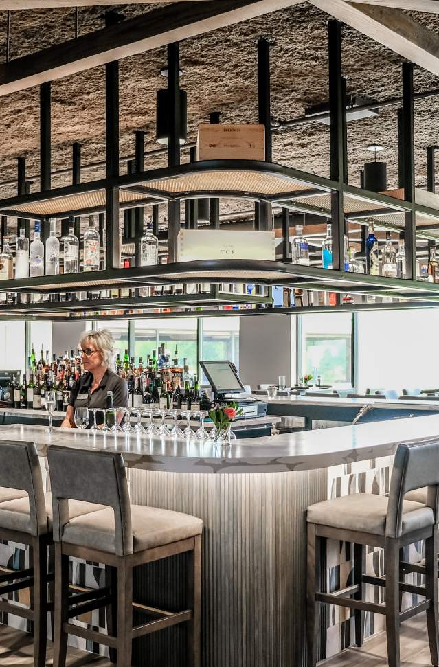 bar with bar stools around, glass wear hanging above bar