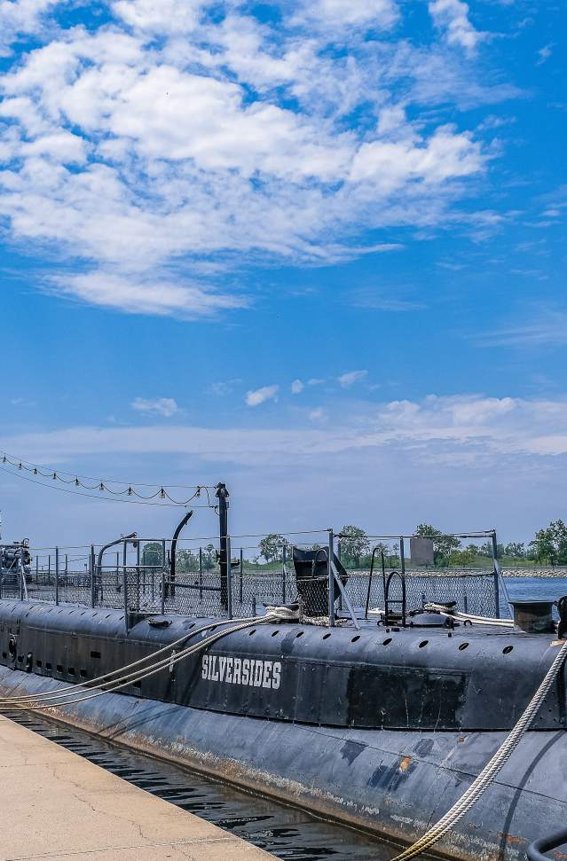 world war II submarine docked in channel. blue skies with white clouds, american flag flying