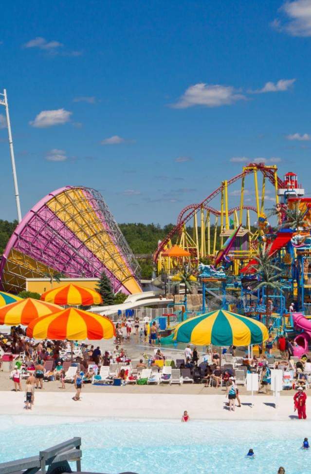 photo of water park, pool with multi color umbrellas and rides in background